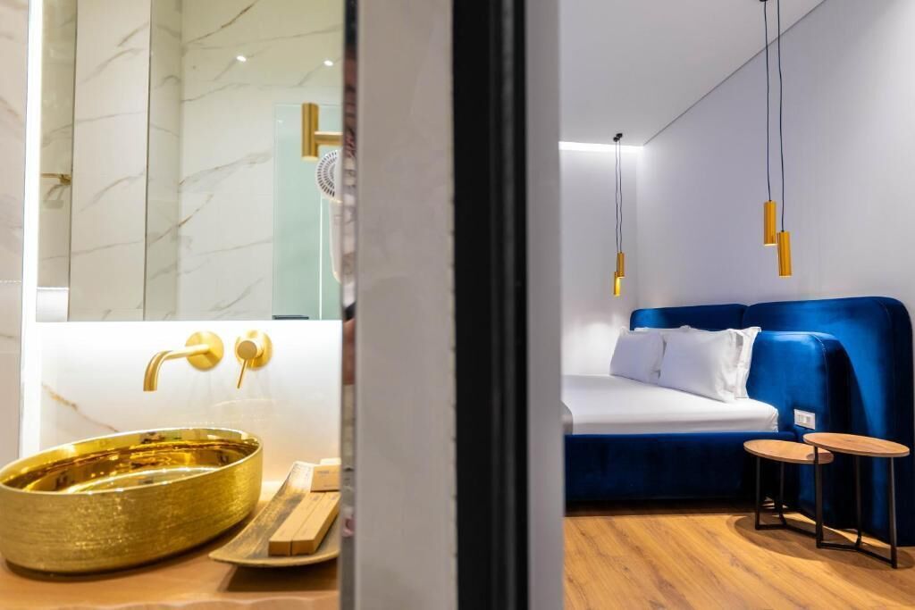 Ein modernes Hotelzimmer mit Marmorbad, einem goldfarbenen Waschbecken, einem blauen Sofa und hängenden Pendelleuchten.