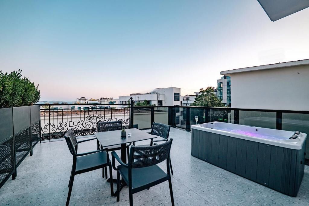 A rooftop terrace with a hot tub, a table with chairs, and a view of the cityscape.