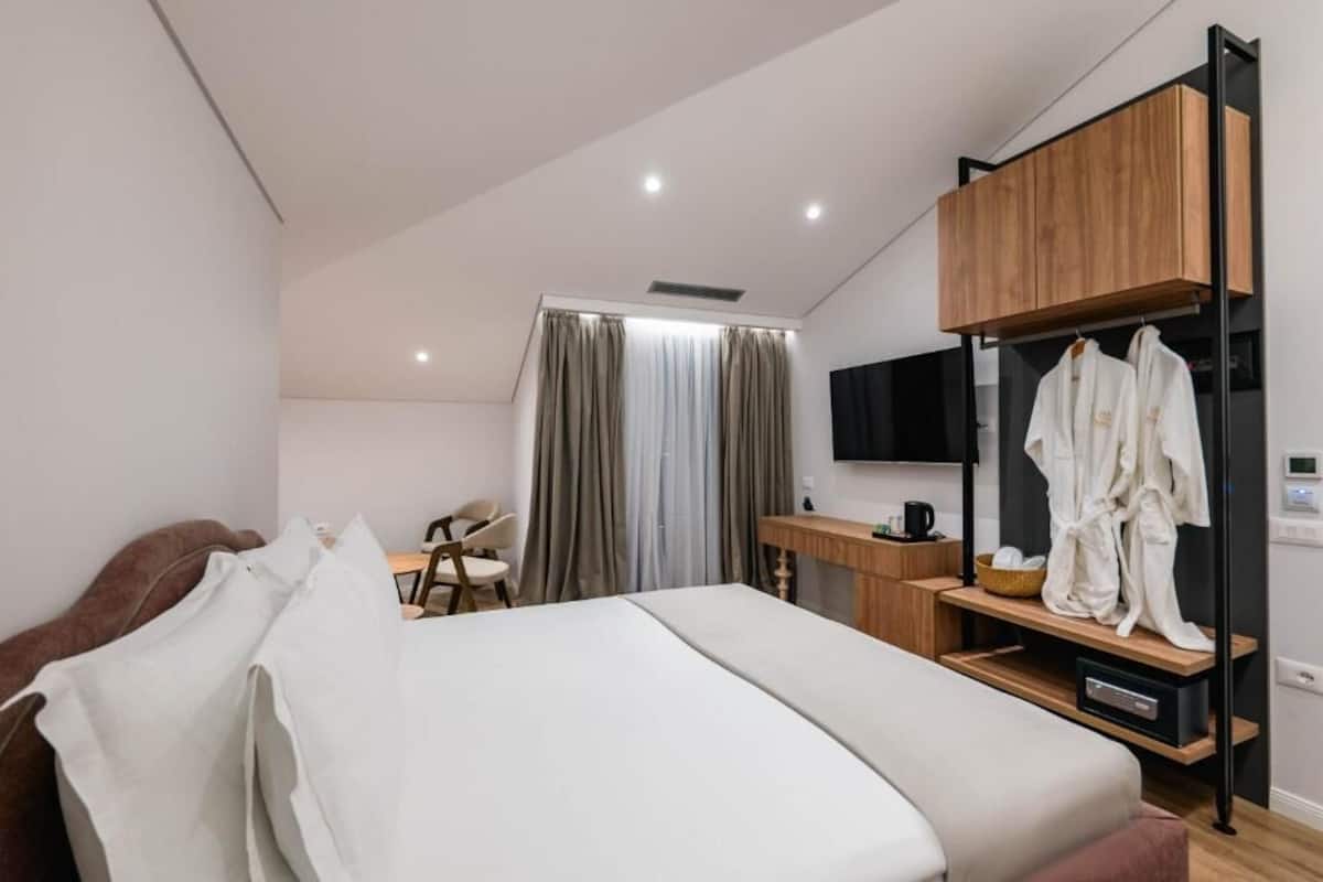 A modern hotel room with a bed, a desk, a chair, a TV, and a wardrobe.