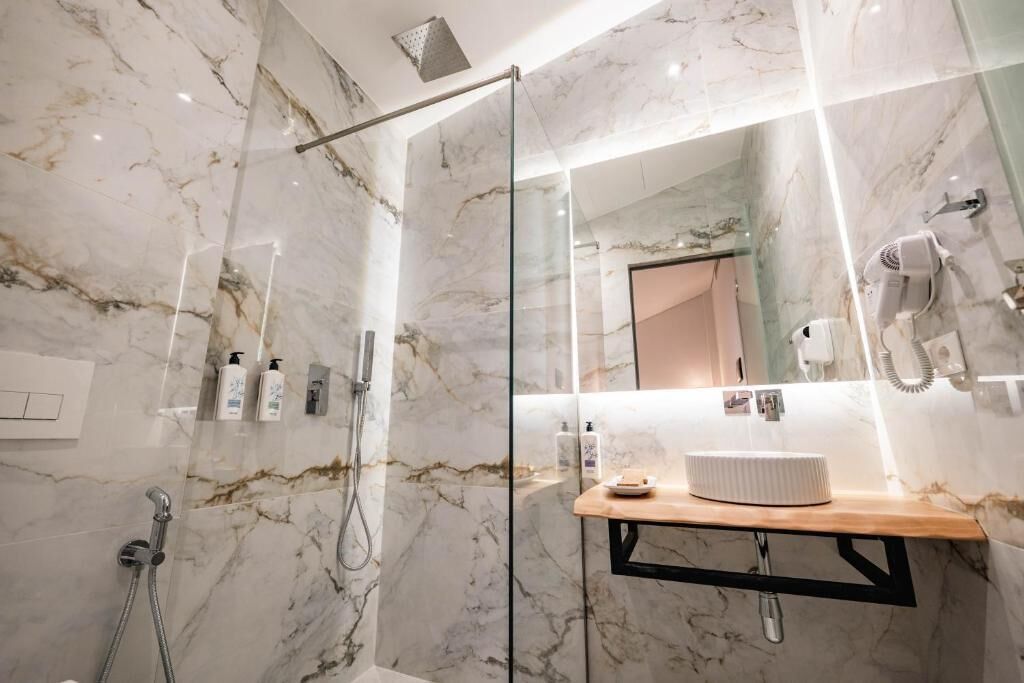 Un bagno moderno con pavimento in marmo, doccia vetrata, mobile lavabo in legno e uno specchio grande.