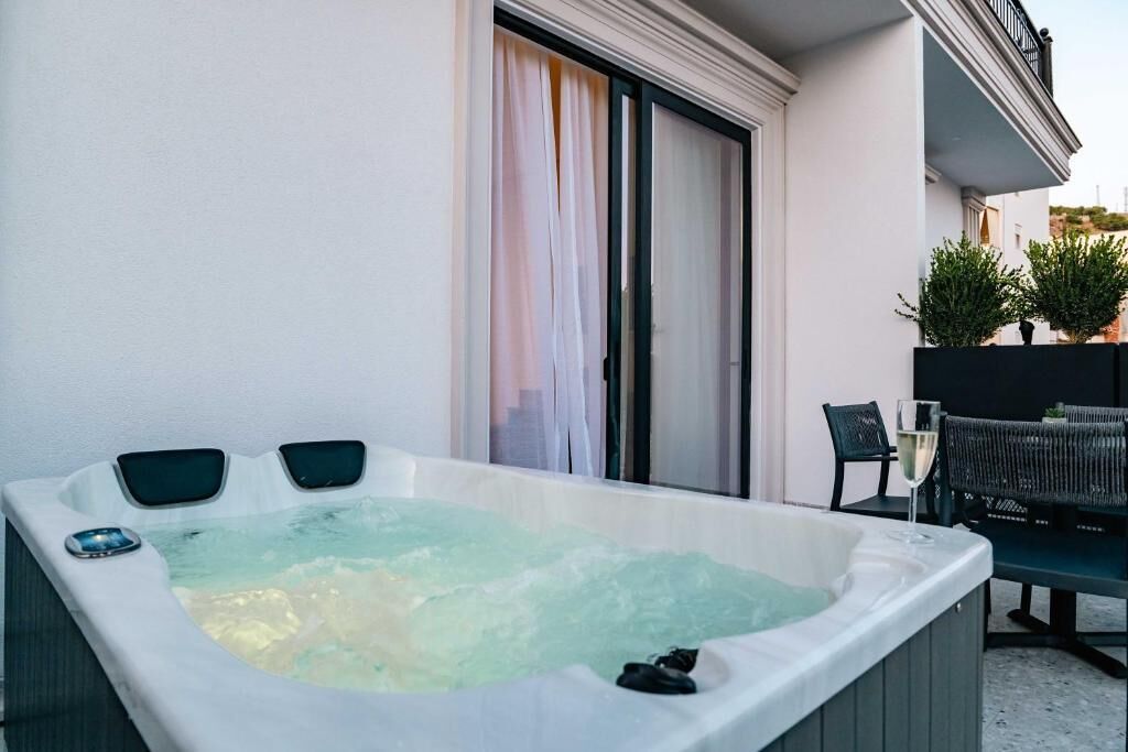 A hot tub on a balcony with a sliding door, a chair, and a glass of wine.