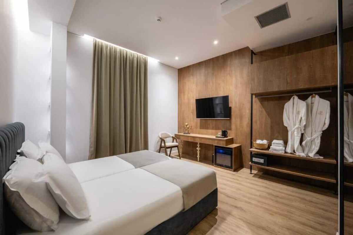 A modern hotel room with a large bed, a desk with a flat-screen TV, a wardrobe, and a seating area.