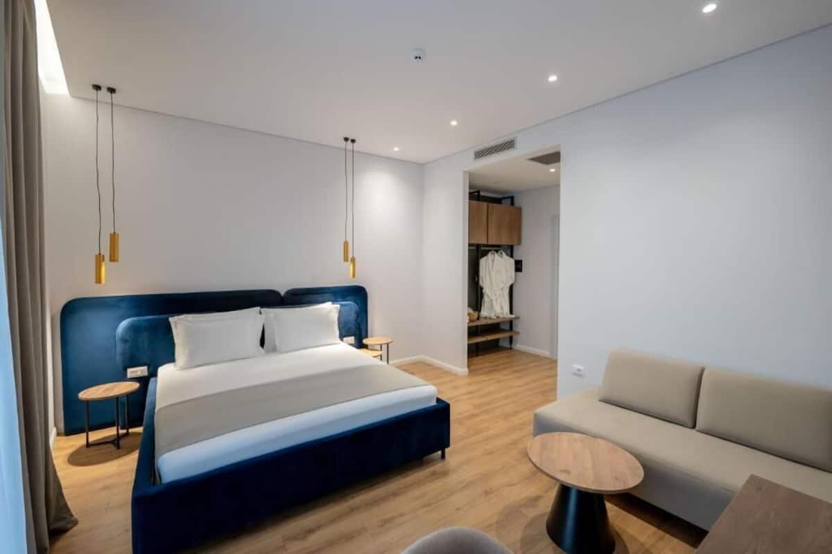 A modern hotel room with a large bed, a sofa, a small round table, and a wardrobe.