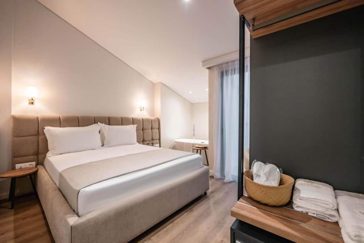 A modern hotel room with a large bed, a small table, and a vanity with a mirror.
