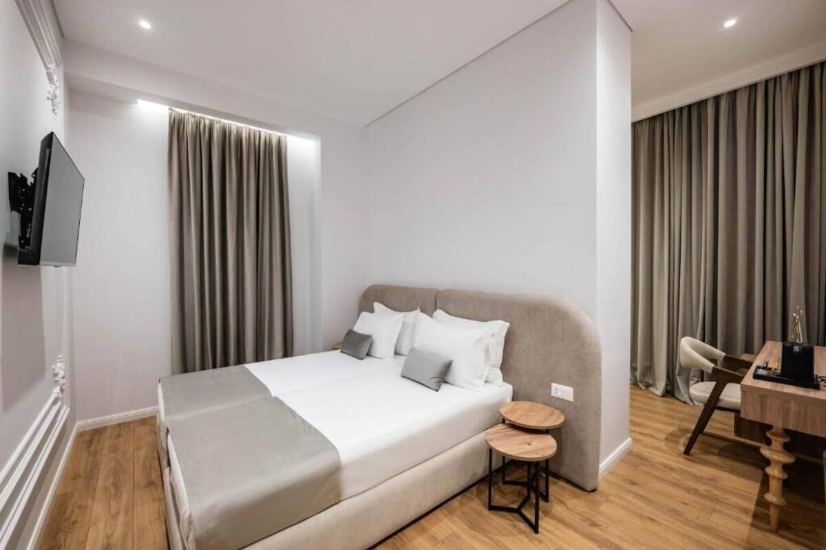 A modern hotel room with a large bed, a small round table, a chair, and a desk with a computer.