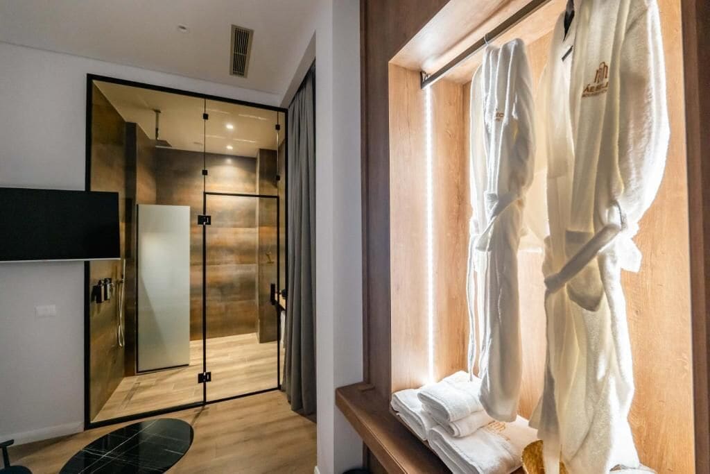 A modern bathroom with a glass shower enclosure, a wooden vanity, and a towel rack by the window.