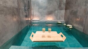Eine Badewanne mit Holztischchen, auf dem zwei Gläser stehen, umgeben von Kerzen und Seerosen.