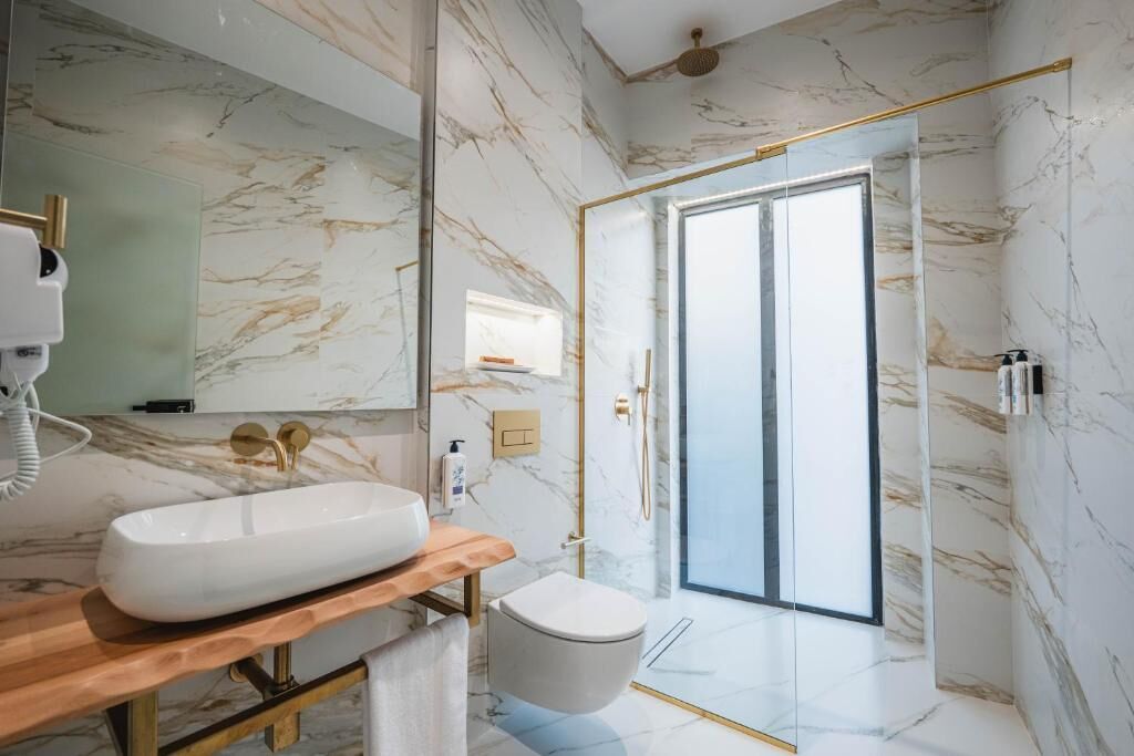 A modern bathroom with a marble wall, a wooden vanity, a white sink, a toilet, and a glass shower enclosure.