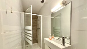 A modern bathroom with a glass shower enclosure, a white sink with a mirror, and a handheld showerhead.