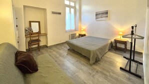 A bedroom with a bed, a chair, a small table, a lamp, and a coat rack. - Luminous T2 on the seafront (Cannes)