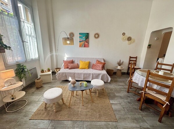 Un salon comprenant un canapé, une table basse et des fauteuils, une table à manger avec des chaises, et une fenêtre donnant sur un beau paysage.