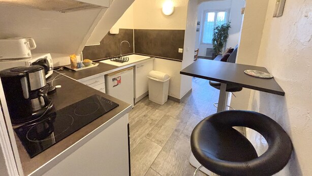 A compact kitchen with a stove, sink, and a small dining area with a chair. - Luminous T2 on the seafront (Cannes)