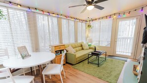 Un salon chaleureux avec un canapé vert, des fauteuils blancs, une table ronde et un ventilateur de plafond.