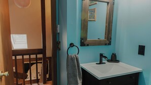 Une salle de bain avec une porte en bois, un lavabo blanc, un miroir et un porte-serviettes.