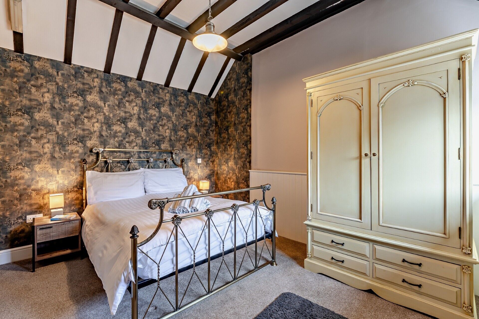 Een slaapkamer met een bed, nachtkastje, lamp, kledingkast en een stenen muur.