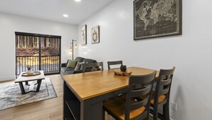 A modern living room with a dining area, a large window with a view of trees, and a world map on the wall. - Juneau Jewel: Luxury & Relaxation A307 (Juneau)