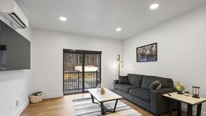 A modern living room with a sofa, a coffee table, a TV, and a balcony with a view. - Luxury Views, Affordable Stay A306 (Juneau)