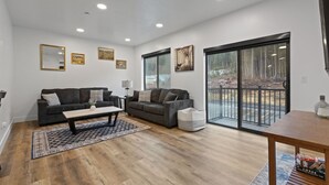 A modern living room with two grey sofas, a coffee table, and a large sliding glass door leading to an outdoor area. - Affordable Luxury With Views!  A305 (Juneau)