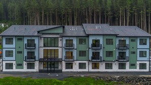 A multi-story building with a central entrance, balconies, and a forested backdrop. - Affordable Luxury With Views!  A305 (Juneau)