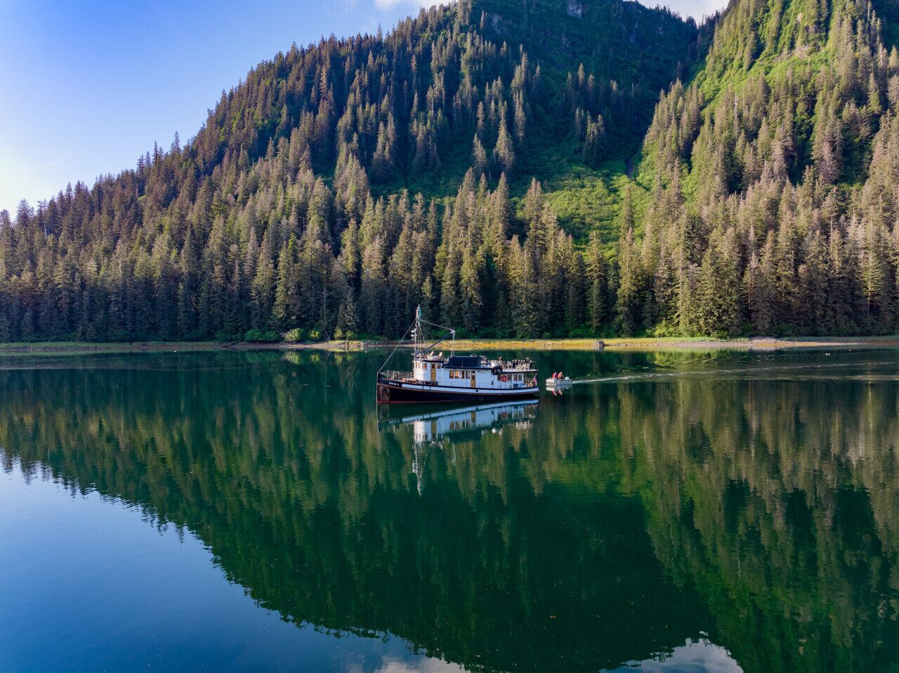 A boat on a calm lake with dense forested hills in the background.