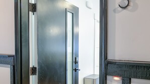 Una puerta moderna con un panel de vidrio, el número '203' de metal en la pared y un piso de madera.