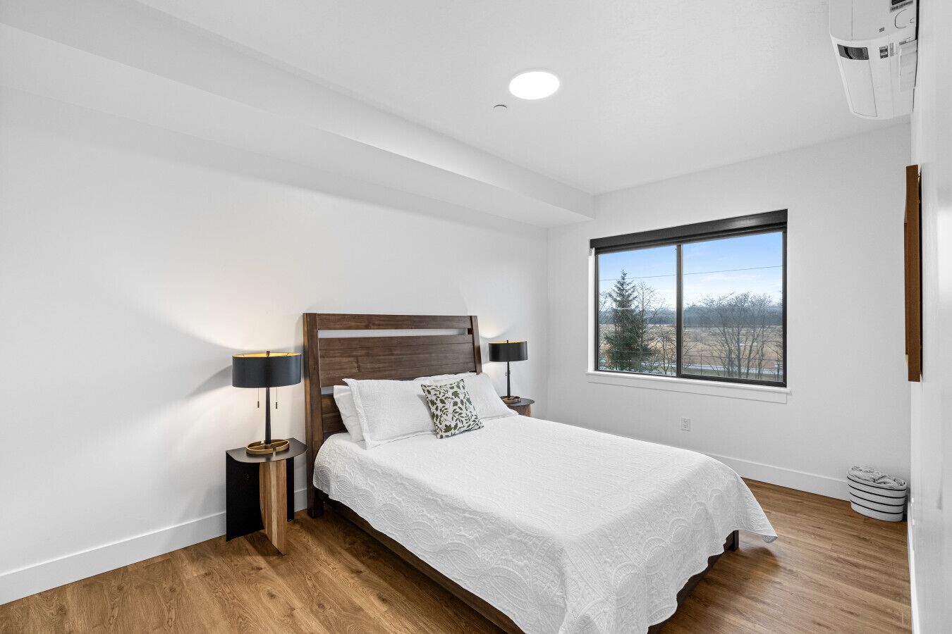 A bedroom with a wooden headboard, a large window, and a bed with white bedding.