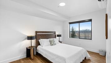A bedroom with a wooden headboard, a large window, and a bed with white bedding.