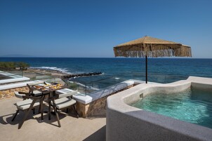Un patio frente al mar con una mesa dispuesta para comer, un jacuzzi y una barandilla de vidrio con vista al océano.