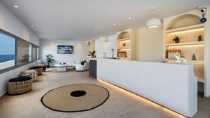 Een moderne hotellobby met een receptie, zithoek en grote ramen met uitzicht op zee.