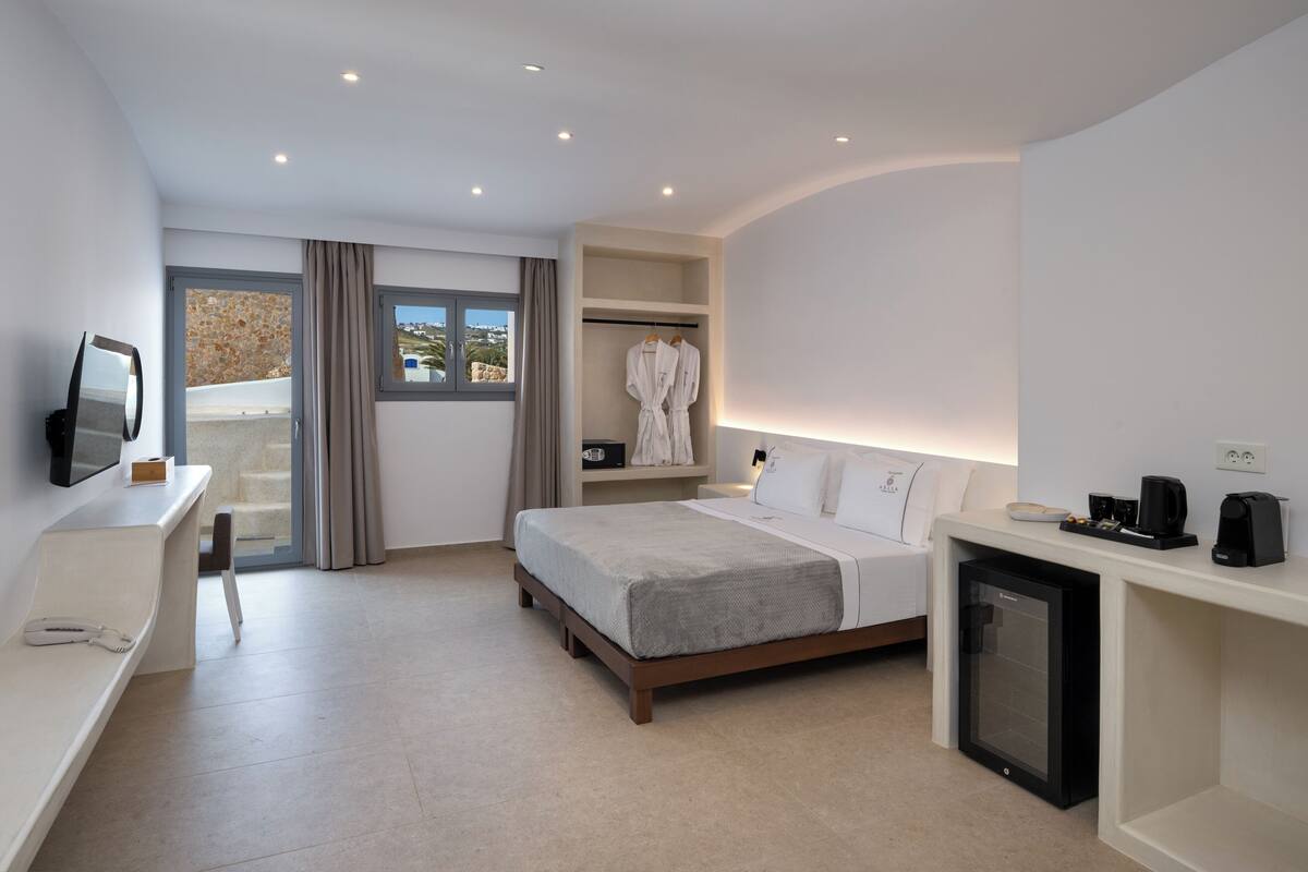 Ein modernes Hotelzimmer mit Bett, Schreibtisch, einem kleinen Kühlschrank und einem Fernseher.