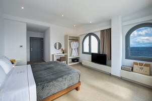 Una habitación de hotel moderna con cama, escritorio con televisor, ventana con vista al mar y un perchero para bata.