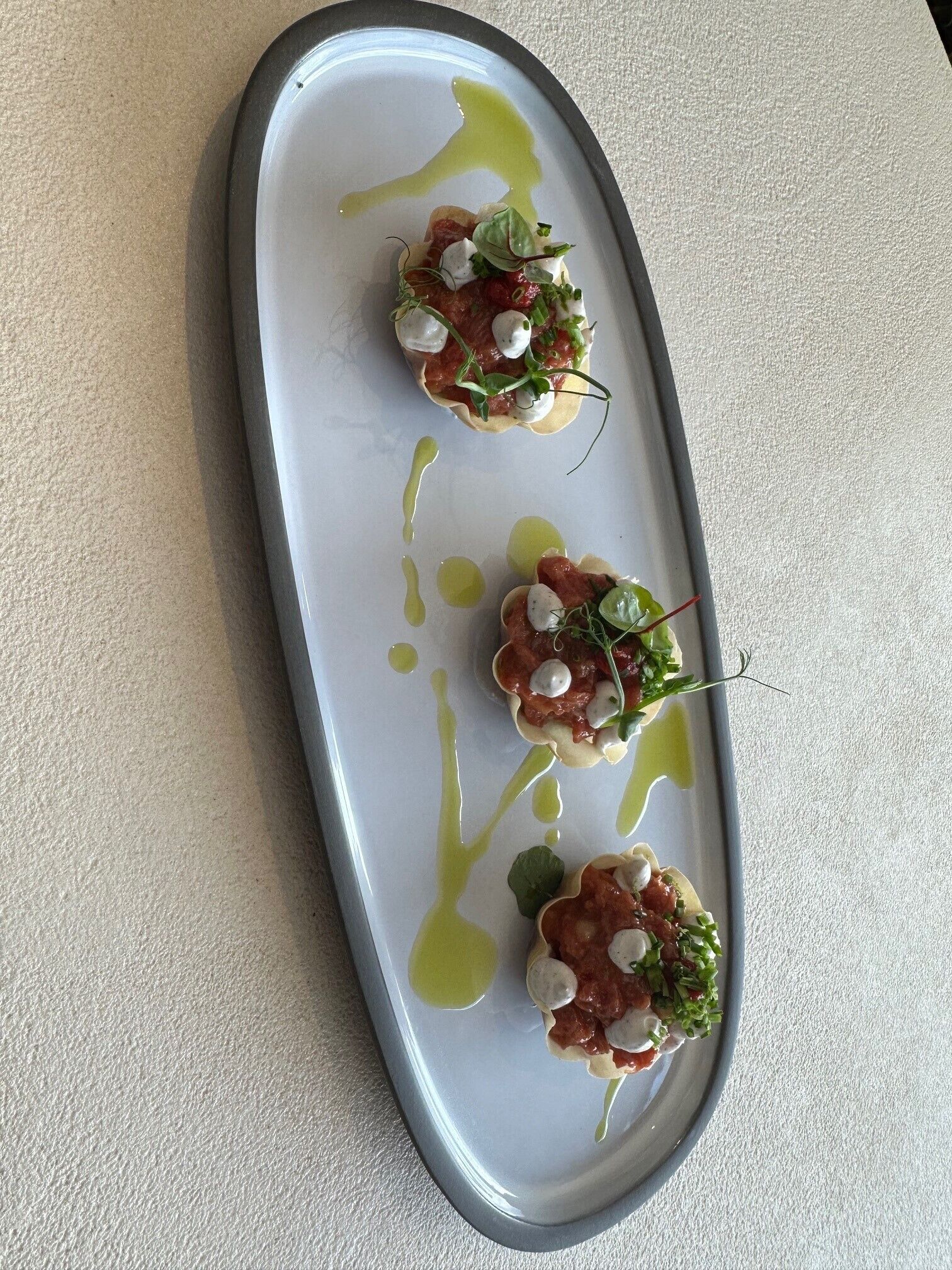 Un plato blanco con tres aperitivos sobre una superficie texturizada.