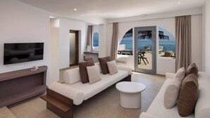 Een moderne hotelkamer met een bank, een televisie, een klein tafeltje en uitzicht op zee door een glazen deur.