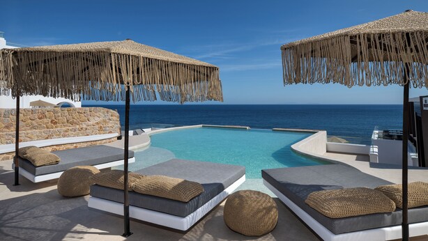 Een zwembadterras met ligbedden en parasols, met uitzicht op een heldere blauwe zee.