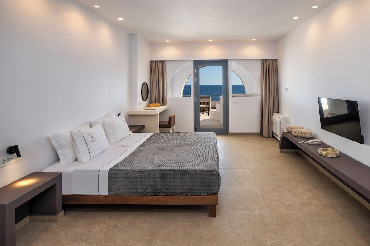 Ein modernes Schlafzimmer mit Bett, Nachttisch, Fernseher und einem Balkon mit Meerblick.