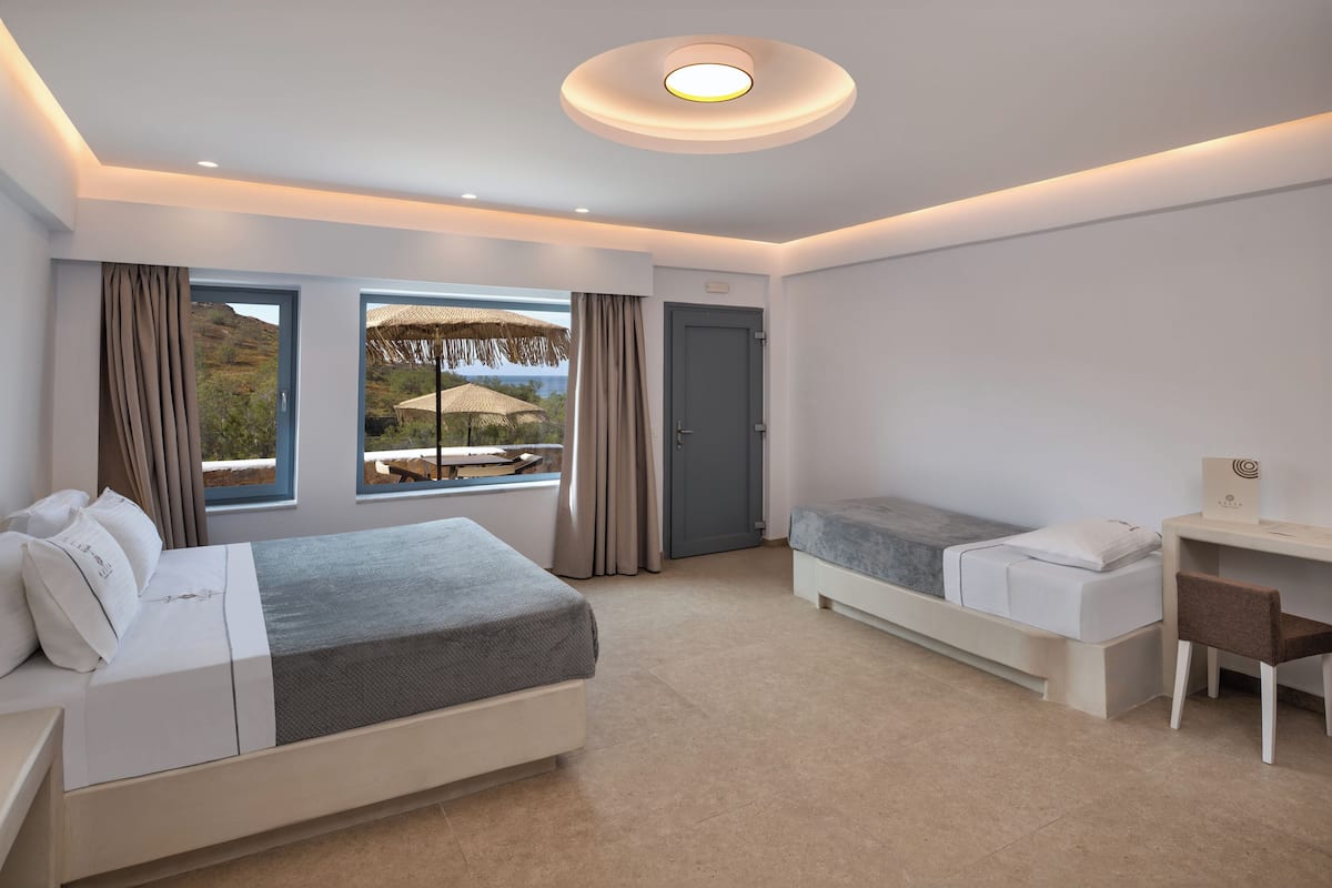 Ein modernes Hotelzimmer mit einem großen Bett, einem kleineren Bett, einem Schreibtisch und Blick ins Freie.