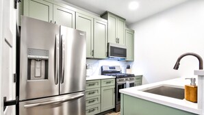 A modern kitchen with stainless steel appliances, green cabinets, a microwave, stove, and a sink with a wooden soap dispenser.