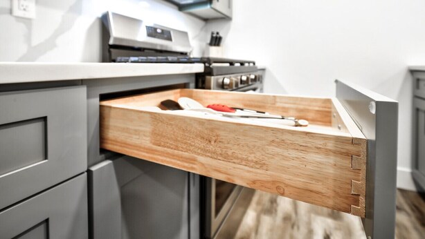 A kitchen with a wooden drawer, a stove, and cabinets.