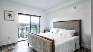 A bedroom with a large bed, a balcony with a view, and a painting on the wall.