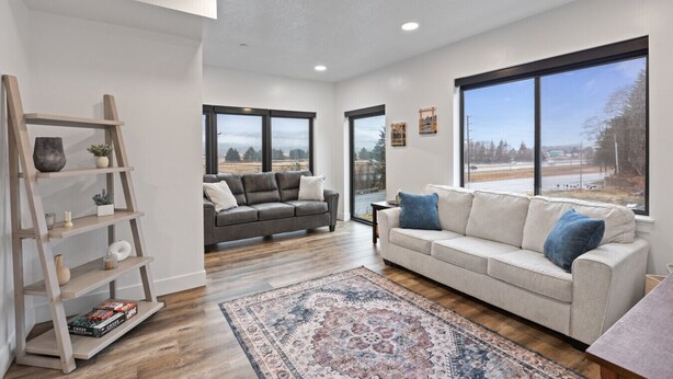 A spacious living room with a grey sofa, a white sofa, a wooden shelf, and large windows offering a view of the outdoors. - Gorgeous Views, Cozy Luxury 209 (Juneau)