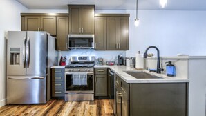 A modern kitchen with stainless steel appliances, wooden cabinets, and a wooden floor. - Cozy, Spacious Retreat with Fireplace 205 (Juneau)