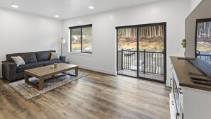 A modern living room with a sofa, coffee table, and a view through a sliding glass door to an outdoor area. - Cozy, Spacious Retreat with Fireplace 205 (Juneau)