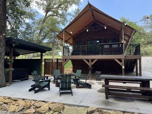 A wooden cabin with outdoor seating, a covered patio, and a balcony overlooking a natural landscape.