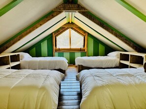 A dormitory room with two beds, a window, and green walls.