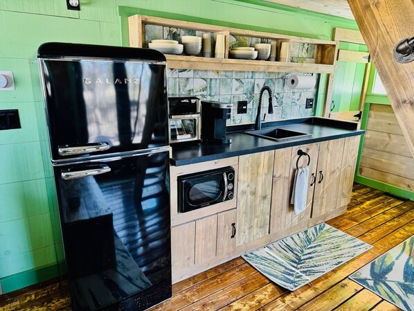 A kitchen with a black Galanz refrigerator, a Keurig coffee maker, a microwave, and a sink.
