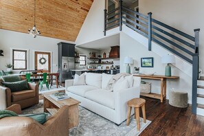 Amplia sala de estar con techo alto, una escalera y una cocina al fondo.