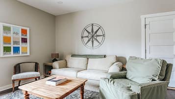 Een woonkamer met een bank, fauteuils, een salontafel, een aan de muur bevestigd kompas en een inlijsting stadsgezicht.
