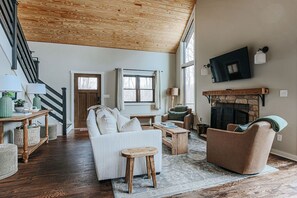 Ein geräumiges Wohnzimmer mit hoher Decke, Kamin, Fernseher und einer Treppe.