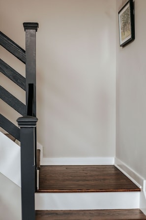 Una escalera con escalones de madera oscura y barandillas negras, que conduce a una pared blanca con un cuadro enmarcado.