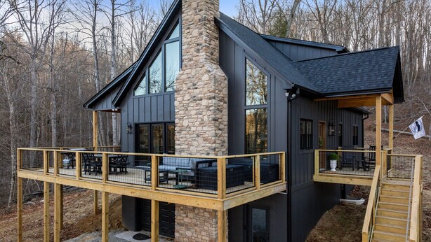 Una casa moderna con chimenea de piedra, ventanas amplias, una terraza de madera y una escalera.